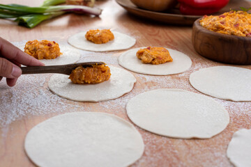Empanadas tapas on wooden board and stuffed with vegetables and squash with bowl and flour preparation for Argentine empanadas
