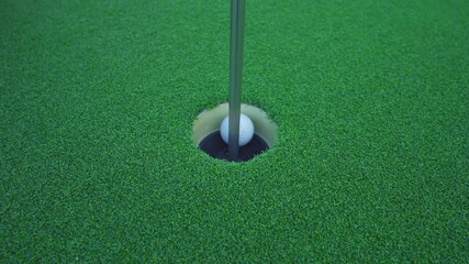 Close up golf ball in hole on grass in golf club, simulation court sport equipment set outdoor activity. People lifestyle.