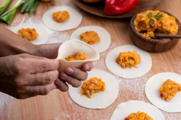 hands making the repulgue and closing of homemade Argentine empanadas and in the background empanadas finished with vegetables and filling on wooden table