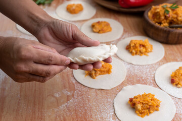 hands making the repulgue and closing of homemade Argentine empanadas and in the background empanadas finished with vegetables and filling on wooden table