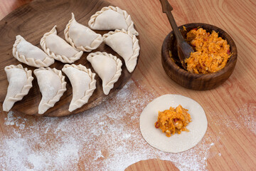 Argentine raw empanadas on round wooden plate on wooden table top with flour decorated with vegetables