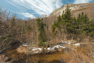 A large mountain in the spring against a bright cloudy blue sky beautiful landscape photo of nature with a stream running water in front.