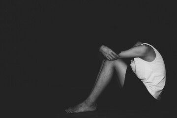 Sad child sitting on floor in dark room, black and white image