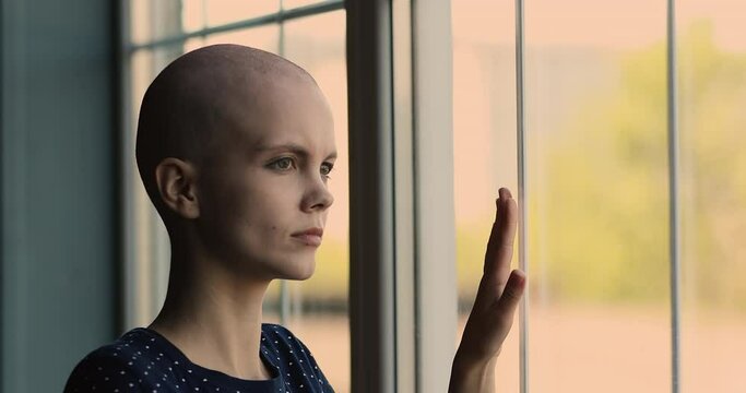 Unhappy stressed young caucasian woman with hairless head after chemotherapy looking in distance out of window, thinking of cancer recurrence or ineffective illness treatment, feeling depressed.