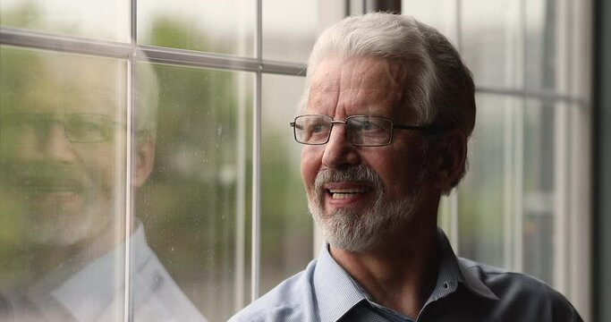 Smiling happy older senior retired hoary man in eyeglasses looking out of window, enjoying peaceful calm moment, meditating breathing fresh air, recollecting good memories, feeling cheerful, headshot.