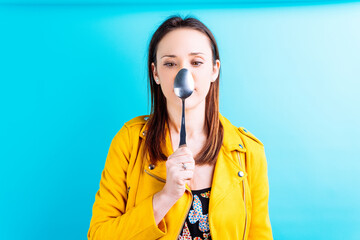 beautiful young woman in yellow jacket on blue background with a spoon covering her nose....