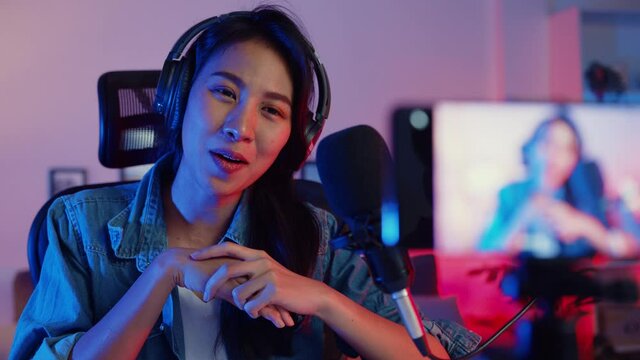 Happy asia girl blogger music influencer use smartphone broadcast recording wear headphone online live talk with listening audience in living room home studio at night. Content creator concept.