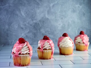 Yellow cupcakes piled high with white frosting and pink drizzle icing with a fresh raspberry on...