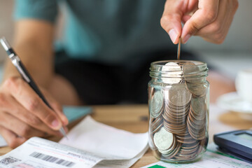 Businessman wearing green t-shirt working on desk office at home and hand holding coins putting in glass.