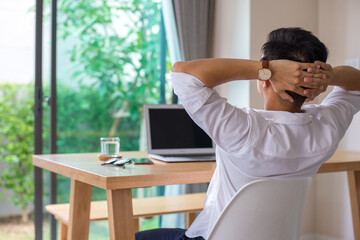 Young asian businessman wearing white shirt sitting at your desk Clasp your hands on the back of your head at home suffering from headache desperate and stressed because pain and migraine.