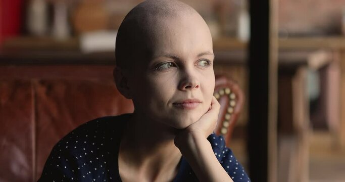 Head shot sincere smiling young hairless after oncology treatment woman thinking of effective illness treatment, visualizing healthy future, feeling hope and inner strength for fighting with disease.