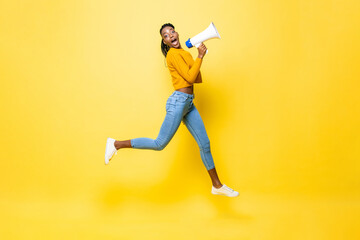 Jumping portrait of shocked young African American woman holding megaphone making announcement in...