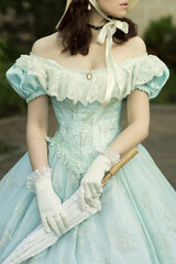 A beautiful young woman in a historical blue dress with an umbrella, gloves and a hat. Dress on a woman of the 19th century. Design for the book cover © daryakomarova