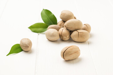 Bright green leaves and pecans on a white wooden table.