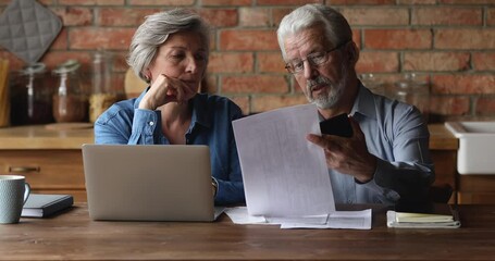 Serious older husband showing banking paper document bills taxes to confused elderly wife, sharing financial problems at home. Stressed middle aged family couple calculating expenses together indoors. - Powered by Adobe