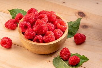 Raspberry fruit in tiny wooden bowl on Wooden background, Raspberries with leaves on Wooden background.