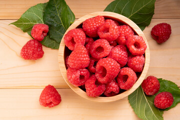 Raspberry fruit in tiny wooden bowl on Wooden background, Raspberries with leaves on Wooden background.