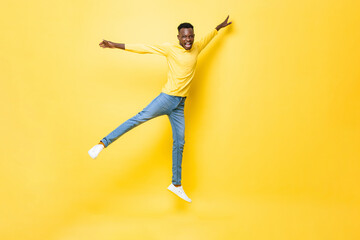 Fototapeta na wymiar Young happy energetic African man jumping with open arms and legs on isolated yellow studio background