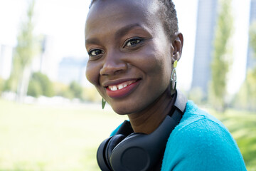 black african woman looking directly at kla camrea with a wireless headset on her neck with a smile on her face, close up