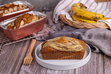 Homemade banana bread topping with banana slice on white plate.