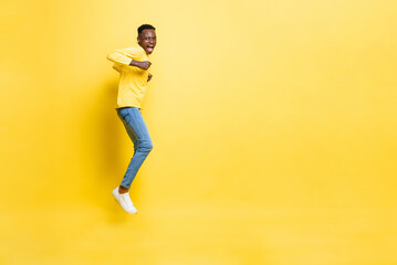Fototapeta na wymiar Young cheerful excited African man jumping with hands clenching on isolated yellow studio background with copy space