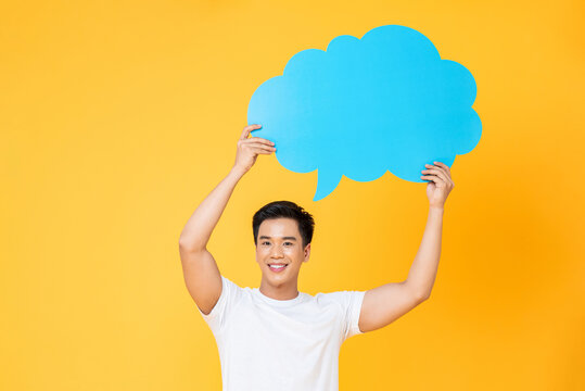 Smiling young handsome Asian man holding speech bubble with empty space for text on colorful yellow background