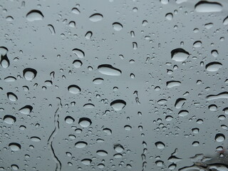 Round, clear rain droplets hitting the front windshield of the car.