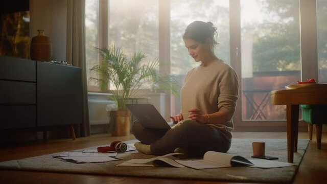 Young Woman Using Laptop at Home, Does Remote Work. Beautiful Smiling Girl Sitting on the Floor Works with Papers, Documents, Brainstorms Project with Research. Productive Work in Sunny Living Room