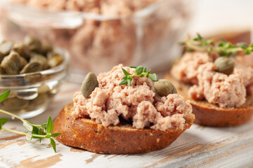 Fresh homemade goose liver pate on toasted bread with greens and capers.