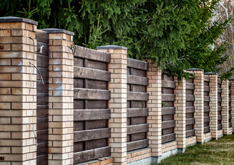 A fence around the territory of a private house made of bricks and boards.