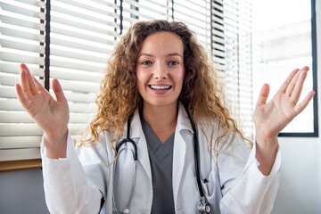 Happy young Caucasian woman doctor looking at camera and explaining patient while making online...