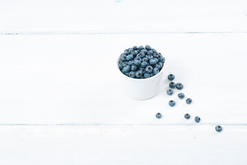Fototapeta na wymiar bilberry fruits at white ceramic cup, on bright wood table