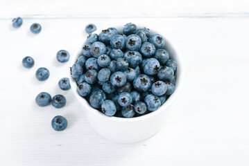 bilberry fruits at white ceramic cup, on bright wood table