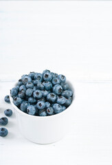 bilberry fruits at white ceramic cup, on bright wood table