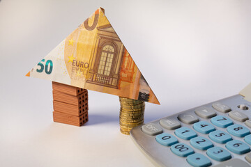 House made of brick and coins stacks with a 50 euro note as a roof and a calculator. Home loan real estate for mortgage concept
