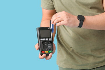 Young man with payment terminal and credit card on color background, closeup