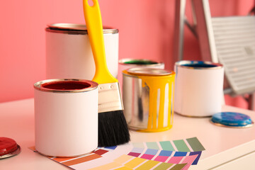Cans of paints with tools on table near color wall, closeup
