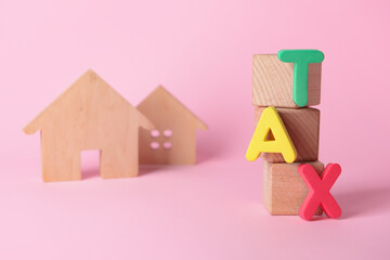 Cubes with word TAX and figures of houses on color background