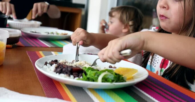 Little girl eating lunch feijoada, child holding fork and knife eating meal