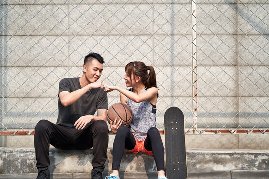 young asian man and woman bumping fists outdoors