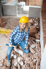 pretty young worker woman with blue work shirt and yellow protective helmet works on construction site and holds hammer in her hand, concept of female worker