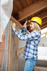 pretty young worker woman with blue work shirt and yellow protective helmet works on construction site and holds hammer in her hand, concept of female worker