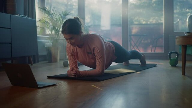 Beautiful Girl Doing Exercising at Home, Watching Tutorial on Laptop. Authentic Plus Size Woman Doing Sport Routine, Fitness Workout, Plank, Stretching Yoga Exercises. Sunny Stylish Living Room