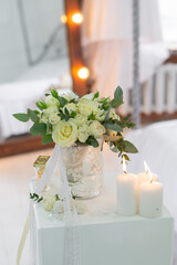 A wedding bouquet of white roses and eucalyptus stands in a vase on the table next to candles and sweets. The bride's morning preparations. Details of a stylish European wedding day