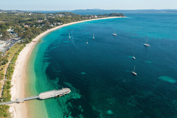 Aerial view of Shoal Bay foreshore and wharf looking west over the aqua waters of Port Stephens, Australia.