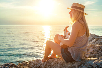 Summer Vacation. Smellingcaucasian women relaxing and playing on ukulele on beach, so happy and luxury in holiday summer, outdoors sunset sky background. Travel and lifestyle Concept.
