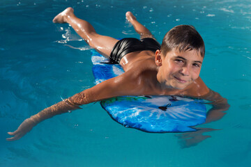teen boy swimming in the pool on the board and smiling, vacation © aneduard