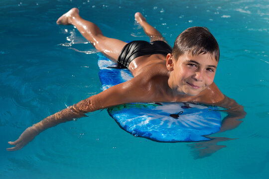 teen boy swimming in the pool on the board and smiling, vacation