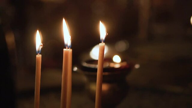 Long thin vax candles burning in the church. Selective focus slow motion shot