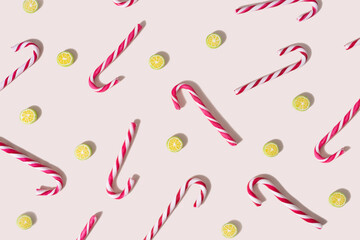 Pattern created of red and white striped candy canes  with hard candy looks like slice of lime. Top view on a light champagne background.